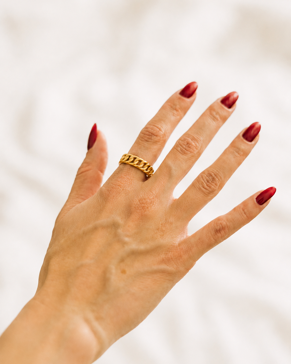 Gold-plated chain ring worn on hand against white fabric