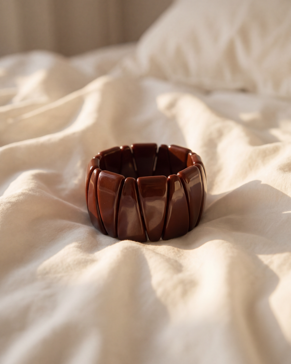 A wide, segmented dark brown wooden bangle bracelet resting on draped cream-colored fabric.
