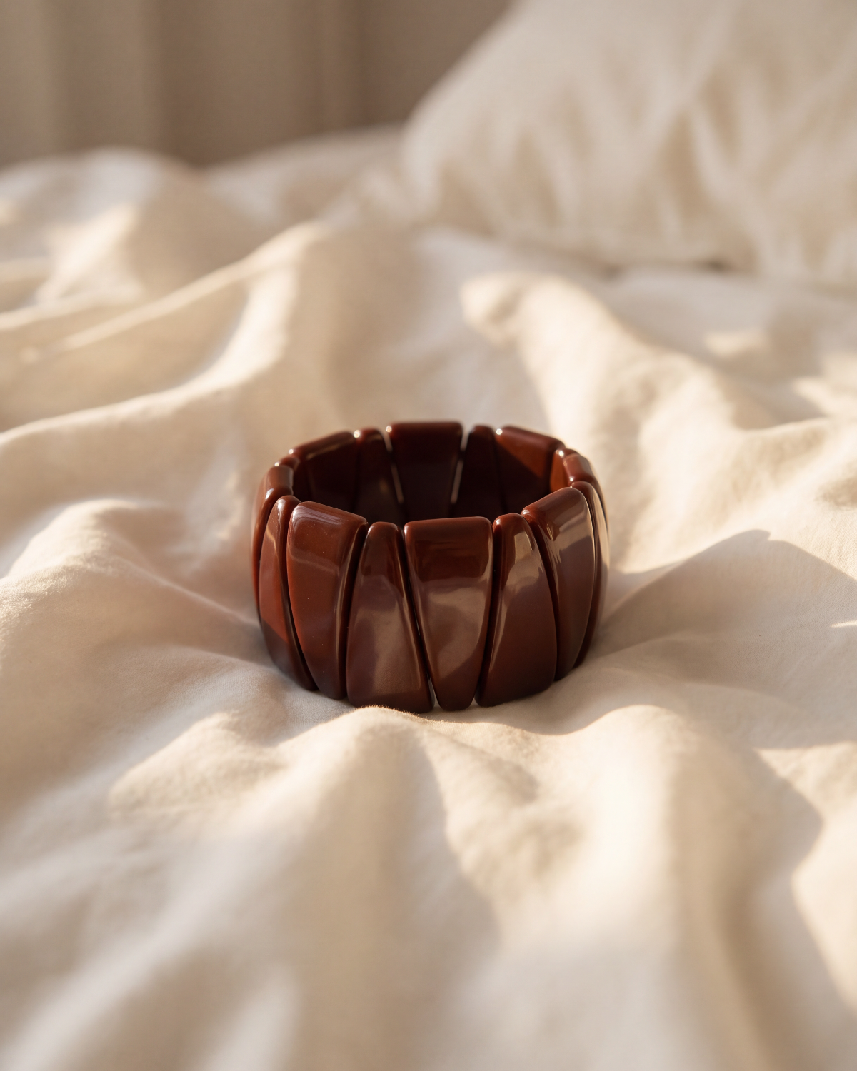 A wide, segmented dark brown wooden bangle bracelet resting on draped cream-colored fabric.