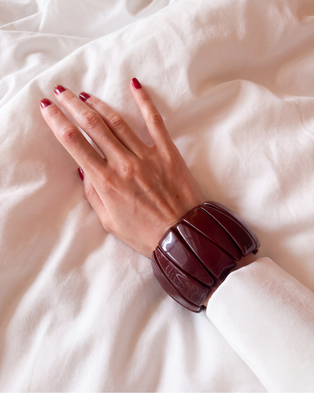 A close-up of a person's hand resting on white fabric, wearing a wide, chunky dark burgundy bracelet.