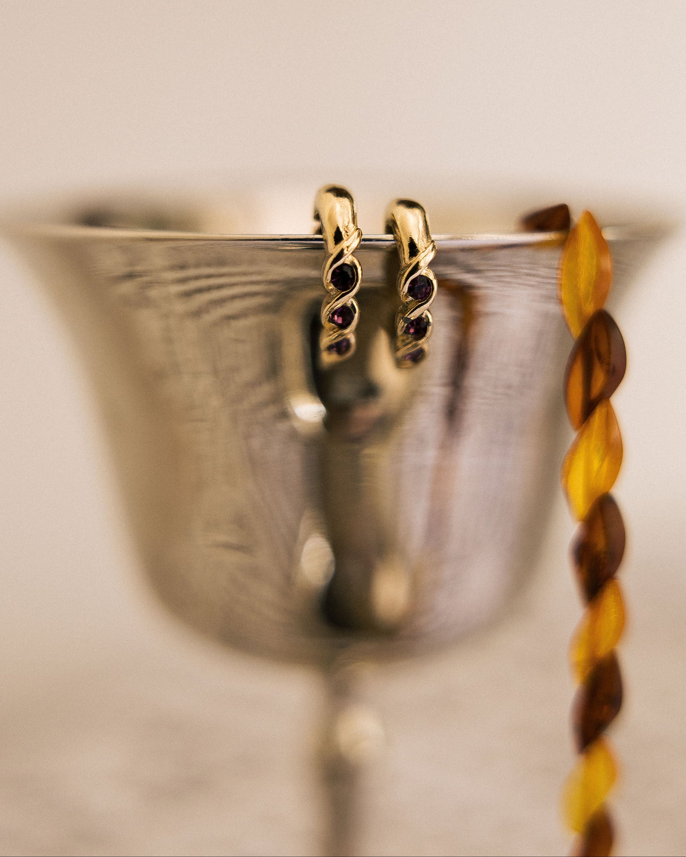 Vintage Amethyst Clip-On Earrings hanging on silver goblet rim with honey necklace beside