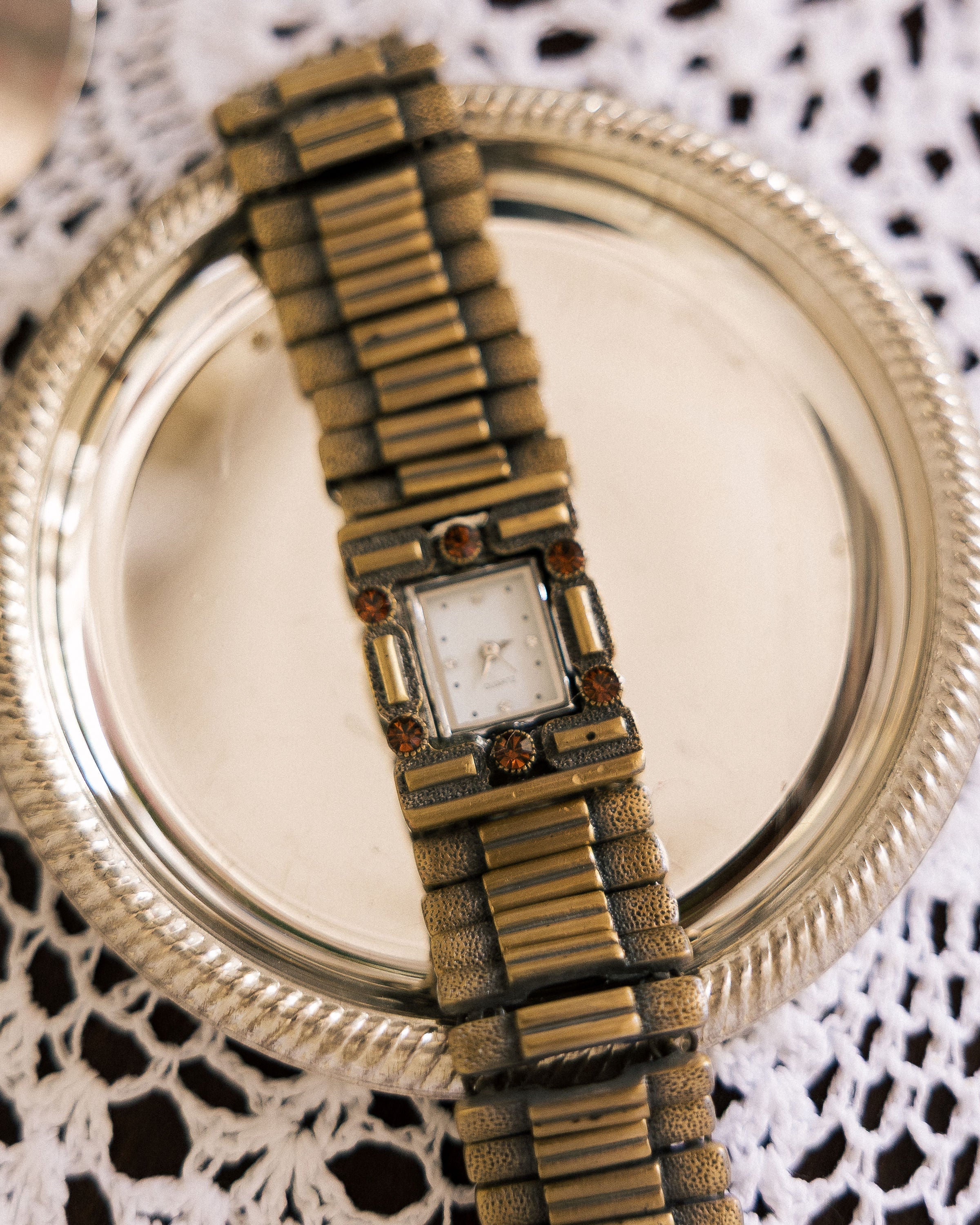 Vintage Watch with antique gold-tone finish and amber crystals on silver tray with lace cloth